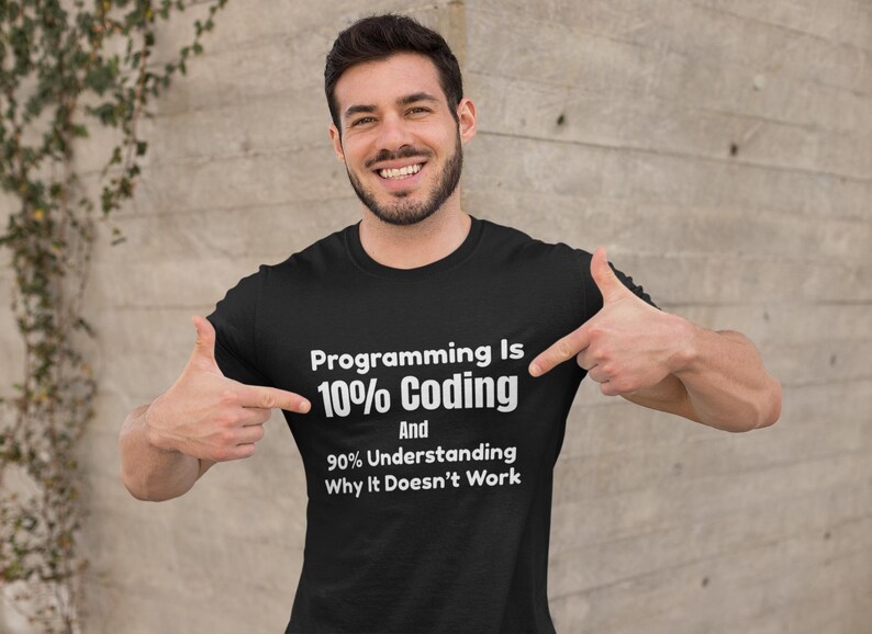 Op de afbeelding: Een zwart t-shirt met korte mouwen en witte tekst die luidt: Programming Is 10% Coding And 90% Understanding Why It Doesn't Work. Het shirt heeft een ronde hals en is gemaakt van effen zwarte stof met duidelijke, witte letters.