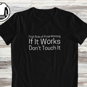May include: Black t-shirt with the text "First Rule of Programming If It Works Don't Touch It" in white. The shirt also features a white and black logo in the upper left corner. The shirt is a crew neck.