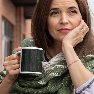 Może przedstawiać: Biały kubek ceramiczny z czarno-zielonym wzorem przedstawiającym kod w stylu macierzy i słowo "NaN".