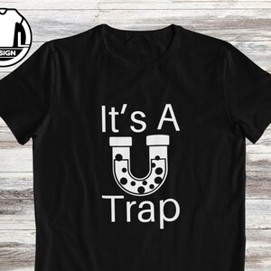 May include: Black t-shirt with white text that reads "It's A U Trap" with a horseshoe-shaped graphic with white dots inside.