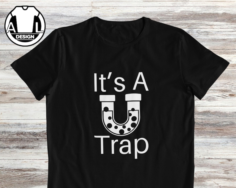 May include: Black t-shirt with white text that reads "It's A U Trap" with a horseshoe-shaped graphic with white dots inside.