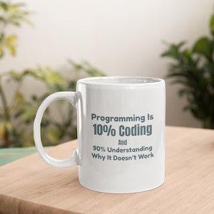 May include: A white ceramic mug with a handle on the left side. The mug features dark gray text that reads: Programming Is 10% Coding And 90% Understanding Why It Doesn't Work. The design is printed clearly on the front surface of the mug.