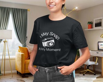 May include: Black t-shirt with the text "I May Snap At Any Moment" and a white camera graphic. The shirt is a crew neck style and is being worn by a person. The person is smiling and has their hands in their pockets.