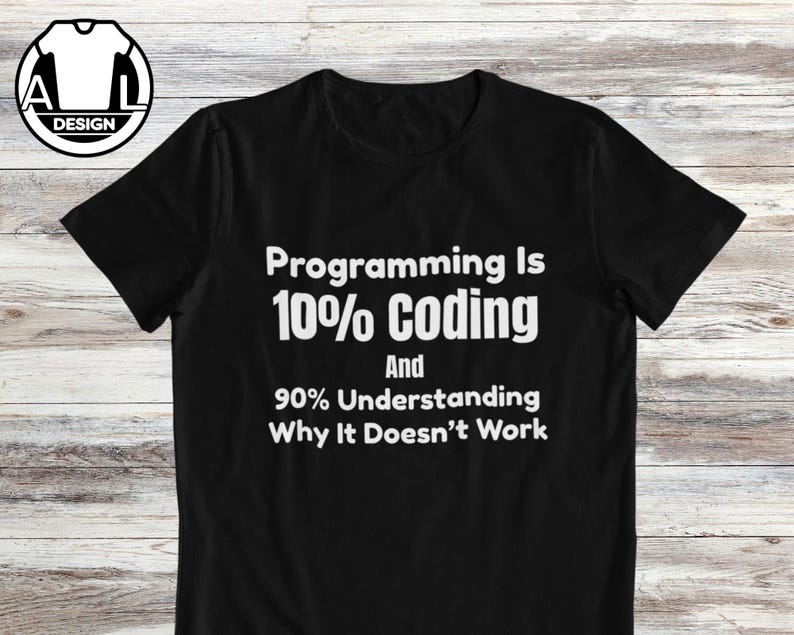 Op de afbeelding: Een zwart T-shirt met korte mouwen en witte tekst: Programming Is 10% Coding And 90% Understanding Why It Doesn't Work. Een cirkelvormig logo met de letters A en L en een T-shirt icoon bevindt zich in de linkerbovenhoek van het kledingstuk.