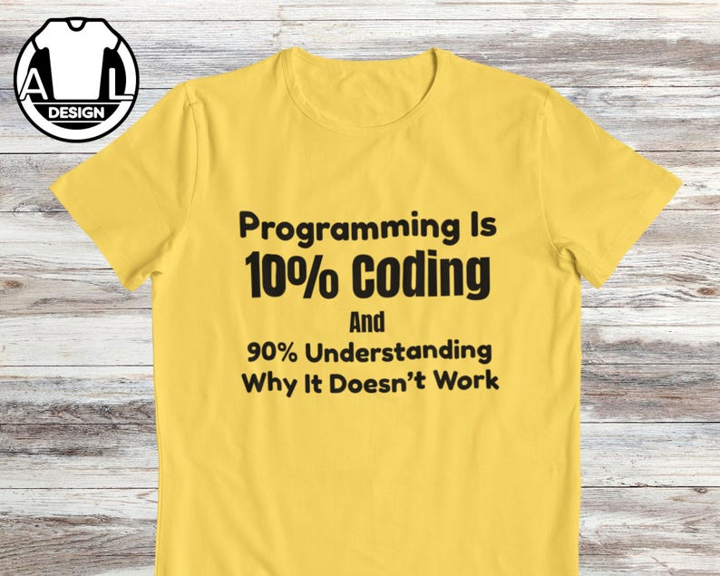Op de afbeelding: Een felgeel T-shirt met korte mouwen en zwarte tekst: Programming Is 10% Coding And 90% Understanding Why It Doesn't Work. Het shirt heeft een ronde hals en ligt plat op een lichtgekleurde houten ondergrond.