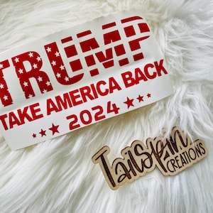 May include: A white decal with the text "TRUMP TAKE AMERICA BACK 2024" in red. The word "TRUMP" has a star-filled design. A wooden tag with the text "Tailspin Creations" is also visible.