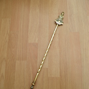 May include: A brass fireplace poker with a twisted handle and a decorative figure at the top. The figure is holding a shovel and has the words "CARTHROSE" and "DUKE" on its base.