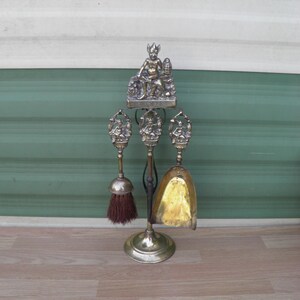 May include: A brass fireplace tool set with a decorative stand featuring a seated figure. The set includes a brush, shovel, and tongs.