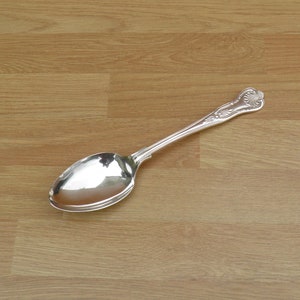 May include: A silver spoon with an ornate handle. The spoon is lying on a wooden surface.