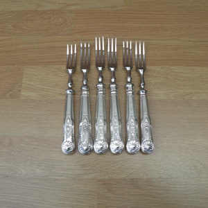 May include: Set of six silver-plated forks with ornate handles. The forks are arranged in a row on a wooden surface.