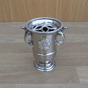 May include: A silver flower vase with a decorative floral design and two handles. The vase has a round base and a cylindrical body.