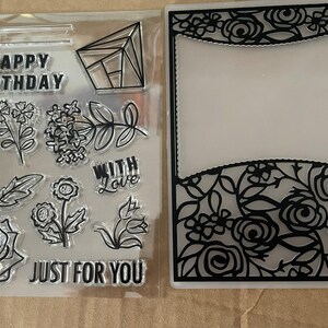 May include: Clear stamps with floral and geometric designs, including a rose, leaves, and the phrases "Happy Birthday," "With Love," and "Just For You." A black floral frame is also included.