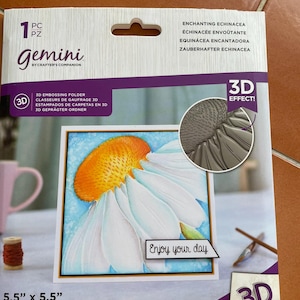 May include: A Gemini 3D embossing folder featuring a detailed daisy design with white petals and an orange center. The package is labeled "Enjoy your day" and measures 5.5" x 5.5".