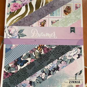 May include: A paper pad with a variety of patterned papers, including floral, butterfly, and animal print designs. The pad features the word "Dreamer" and includes 36 sheets, measuring 6 x 8 inches.