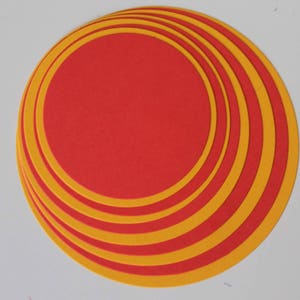 May include: A stack of red and yellow circular paper cutouts. The red circles are layered with yellow rings, creating a spiral effect. The paper has a matte finish and is arranged on a white surface.