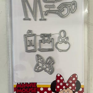 May include: A set of metal die cuts featuring Minnie Mouse, a large letter M, a pair of glasses, a perfume bottle, a bow, and a small purse. The die cuts are packaged on a white card with a red and white polka dot background and the text "Minnie Mouse".