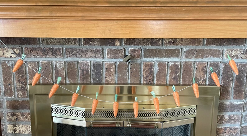 May include: A string of felt carrot decorations hangs above a fireplace. The carrots are orange with green tops and are strung on a white string.