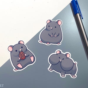K&ouml;nnte beinhalten: Drei graue Hamster-Aufkleber mit wei&szlig;en Umrissen. Ein Hamster h&auml;lt eine braune Nuss, ein anderer steht mit seinen Pfoten zusammen und der dritte Hamster hat seine Backen aufgeblasen.
