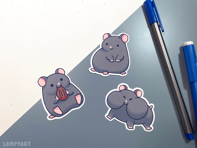 K&ouml;nnte beinhalten: Drei graue Hamster-Aufkleber mit wei&szlig;en Umrissen. Ein Hamster h&auml;lt eine braune Nuss, ein anderer steht mit seinen Pfoten zusammen und der dritte Hamster hat seine Backen aufgeblasen.