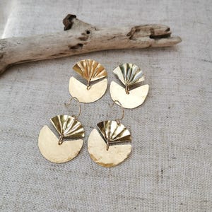 May include: A pair of gold-toned earrings with a geometric design. Each earring features a round, hammered disc with a smaller, fan-shaped piece layered on top.