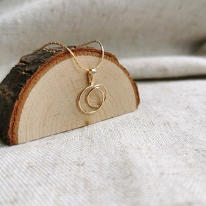 May include: A gold necklace with a double circle pendant. The necklace is on a wooden surface.