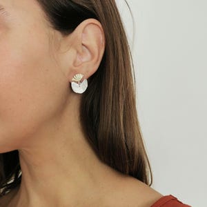 May include: A pair of silver earrings with a gold fan-shaped design. The earrings are small and delicate.