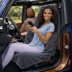 Puede incluir: Una funda de asiento de coche gris oscuro está colocada sobre un asiento de coche marrón. La funda del asiento está hecha de un material suave y absorbente. La funda del asiento del coche está diseñada para proteger el asiento del coche de derrames, manchas y desgaste.