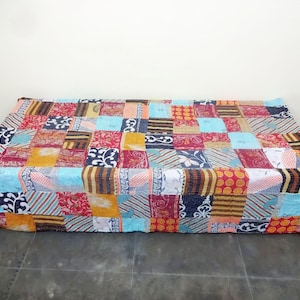 May include: A colorful patchwork quilt made from recycled saris. The quilt is made up of squares of different colors and patterns, including red, blue, yellow, and green. The quilt is perfect for adding a touch of bohemian style to any room.
