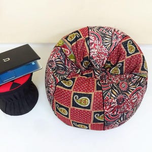 May include: A red, black and green patterned beanbag chair. The chair is round and has a quilted design.