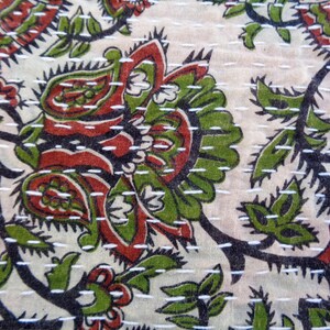 May include: A close-up of a white fabric with a floral pattern in shades of green, red, and black. The fabric is stitched with white thread, creating a quilted effect.