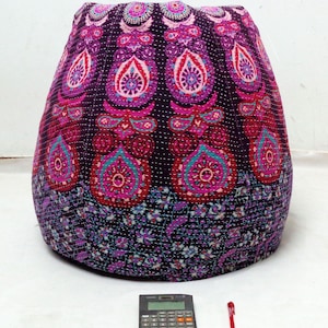 May include: A large, round, purple and pink bean bag chair with a mandala pattern. The chair is made of quilted fabric and has a unique, bohemian style.