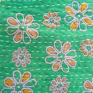 May include: Green fabric with a white and orange floral pattern. The fabric is quilted with white thread.