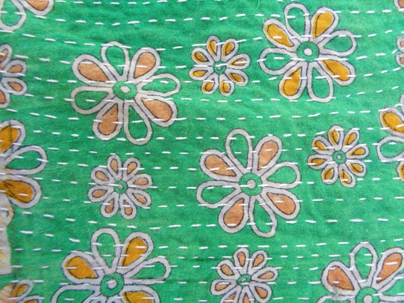 May include: Green fabric with a white and orange floral pattern. The fabric is quilted with white thread.