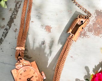Könnte beinhalten: Eine goldfarbene Armbanduhr mit quadratischem Zifferblatt und römischen Ziffern. Die Uhr hat ein zartes Gliederarmband.