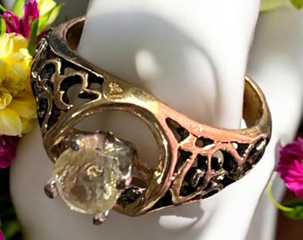 May include: A gold ring with a delicate filigree design and a large, clear, faceted gemstone. The ring is set on a white background.