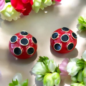 May include: A pair of red and black polka dot earrings. The earrings are round and have a gold rim.