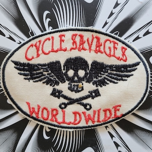Peut inclure: Écusson ovale blanc avec le texte brodé en rouge "CYCLE SAVAGES WORLDWIDE". Un crâne noir avec des ailes et des os croisés se trouve au centre.