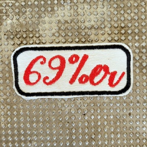 May include: White rectangular patch with a black border. The patch has red embroidered text that reads "69%er".
