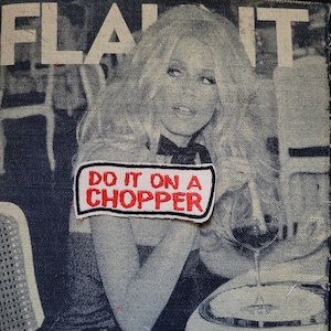 Può includere: Toppa in denim con un'immagine di rivista vintage di una donna e la scritta "FLAUNT IT". Una toppa bianca e rossa con la scritta "DO IT ON A CHOPPER" è cucita sul davanti. L'immagine ha un'estetica vintage.