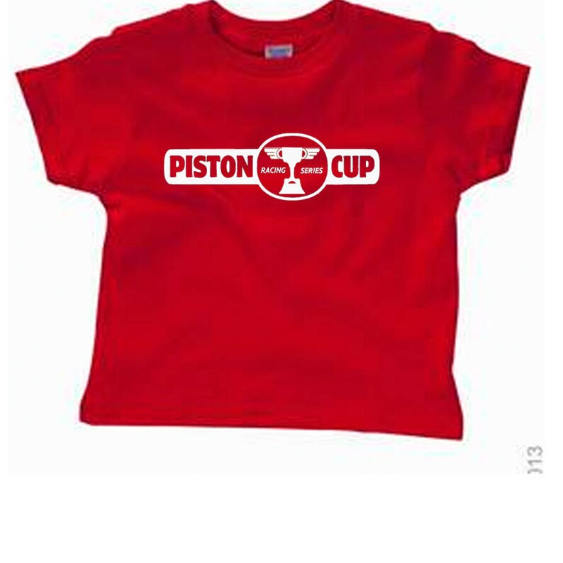 Puede incluir: Camiseta roja con un logotipo blanco de Piston Cup Racing Series. El logotipo presenta un trofeo con alas.