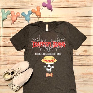 May include: Dark heather grey t-shirt with a black and white graphic of a skull wearing a yellow and red striped hat and a red bow tie. The text "Dapper Dans" is written in a metal band font above the skull. The text "A dream is a wish your heart makes" is written below the skull.