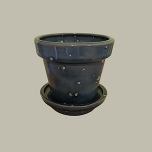 May include: A blue ceramic planter with white speckles and a matching saucer. The planter has a slightly flared rim and a smooth, glazed finish.