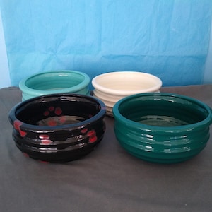 May include: Four ceramic bowls in different colors and patterns. The bowls are round and have a slightly flared lip. The bowls are arranged in a row on a gray surface. The bowls are all different sizes.