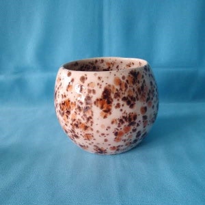 May include: A white ceramic planter with brown and orange speckles. The planter is round and has a smooth, glossy finish.