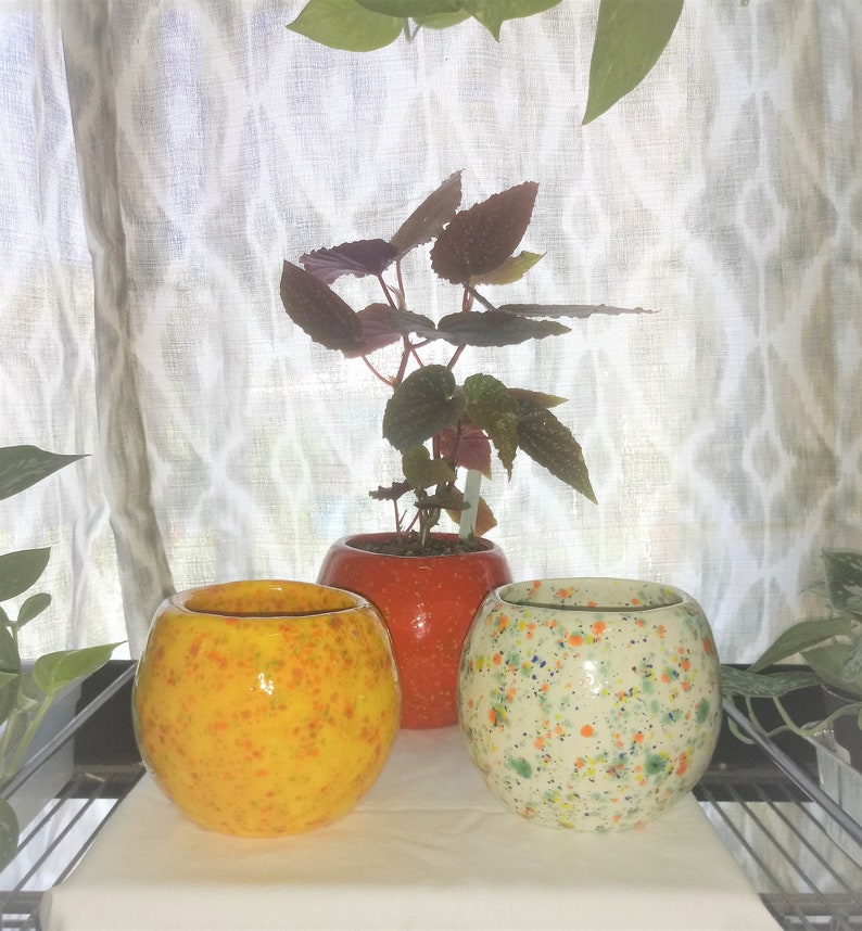 May include: Three ceramic plant pots with speckled patterns. The pots are round and have a glossy finish. The pots are yellow, orange, and white with multi-coloured speckles.