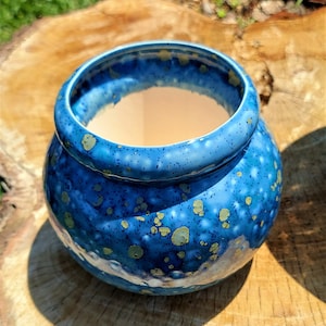 May include: A round, ceramic planter with a vibrant blue glaze and speckled gold accents. The interior is a light beige color. The planter sits on a wooden surface, showcasing its handcrafted details. Perfect for small plants or succulents.