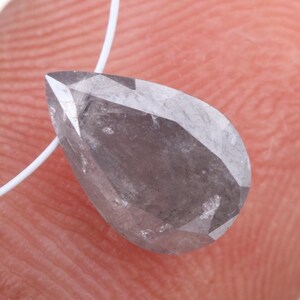 May include: A pear-shaped, gray diamond gemstone with a faceted cut, suspended on a white string.