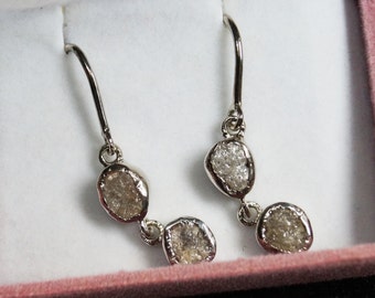 May include: A pair of silver dangle earrings with three rough, clear diamond stones.