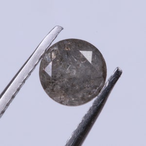 Può includere: Un diamante rotondo grigio con sfaccettature, tenuto da una pinzetta.