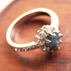 May include: A gold ring with a blue and gray rough diamond set in a halo of smaller diamonds.